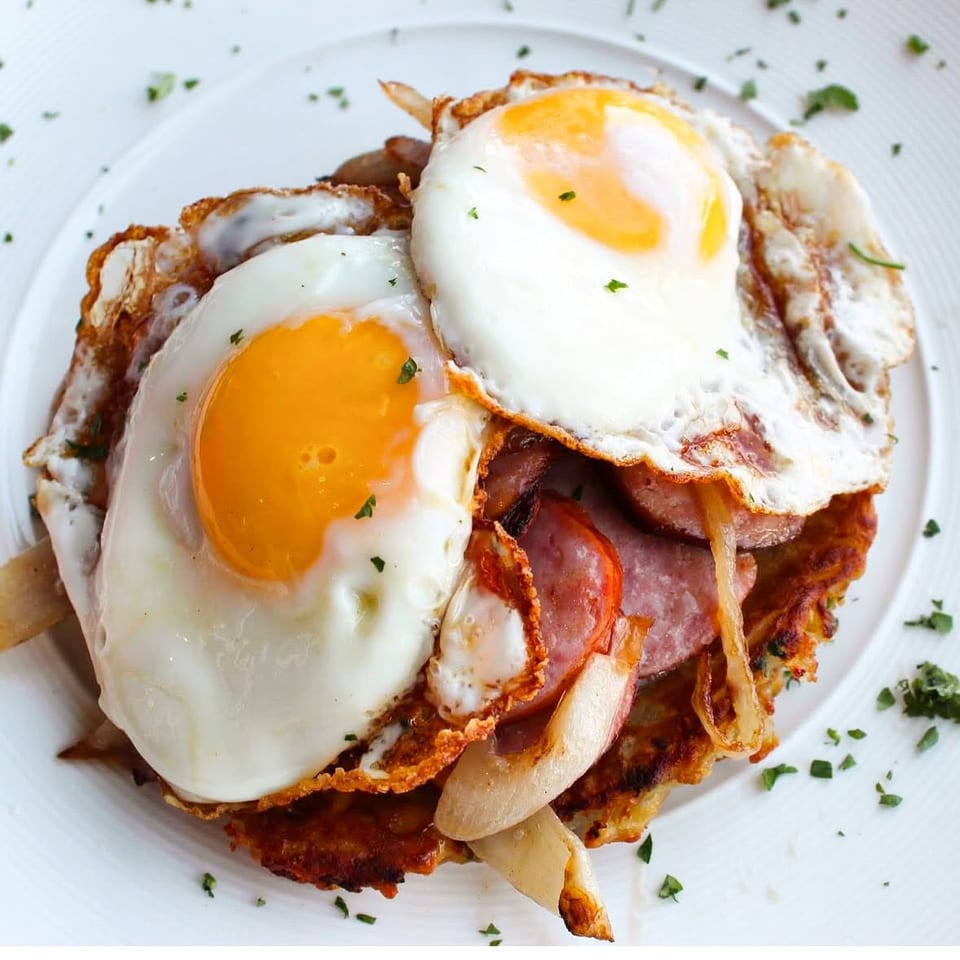 Breakfast topped with two fried eggs, sliced meat, and onions.