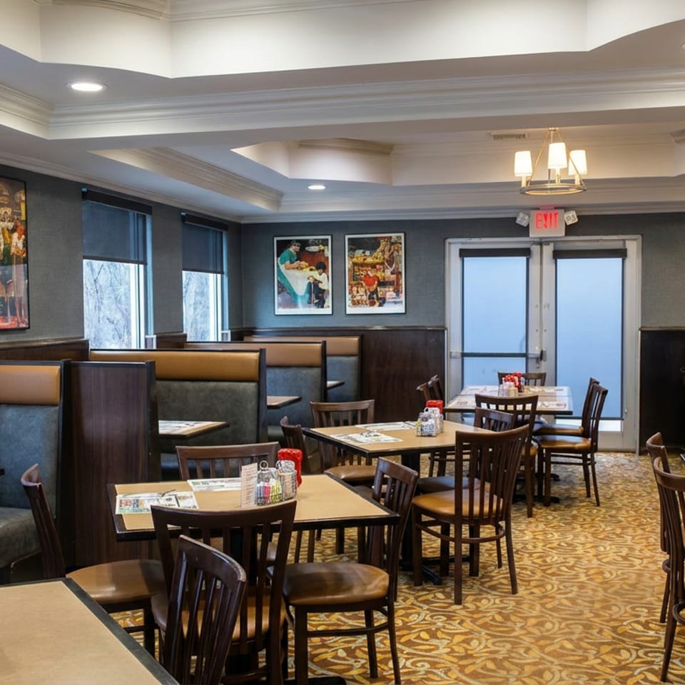 Spacious restaurant dining room with booths, tables, patterned carpet, framed artwork, and illuminated coffered ceilings.
