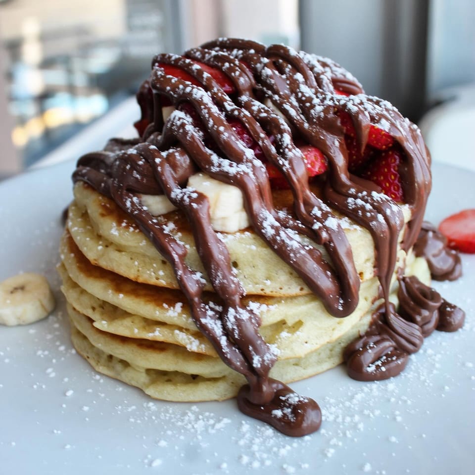 Pancakes topped with strawberries, banana, chocolate spread, and powdered sugar.